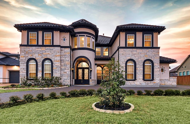 mediterranean / spanish-style home featuring a front lawn, stucco siding, a tile roof, and stone siding