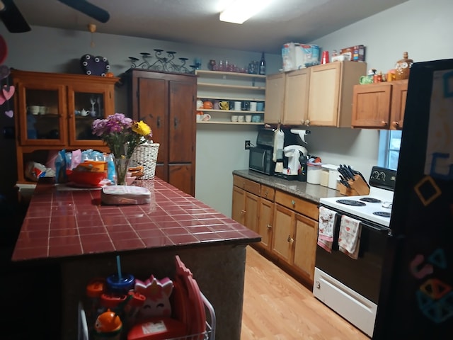 kitchen featuring open shelves, freestanding refrigerator, tile countertops, light wood-type flooring, and range with electric stovetop