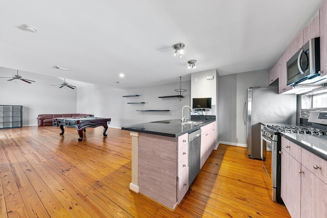 kitchen featuring a peninsula, open floor plan, a sink, light wood finished floors, and appliances with stainless steel finishes