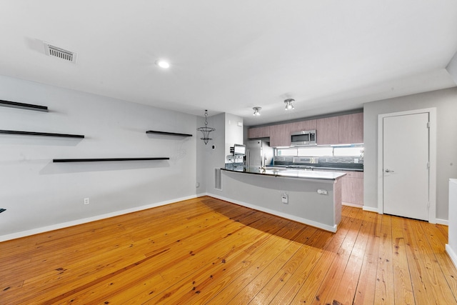 kitchen with appliances with stainless steel finishes, light wood-style flooring, a peninsula, baseboards, and visible vents