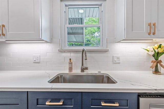 kitchen with light stone counters, a sink, decorative backsplash, and blue cabinets