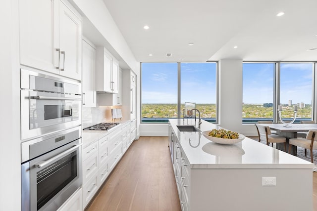 kitchen with a kitchen island with sink, light wood-style floors, recessed lighting, a sink, and stainless steel appliances