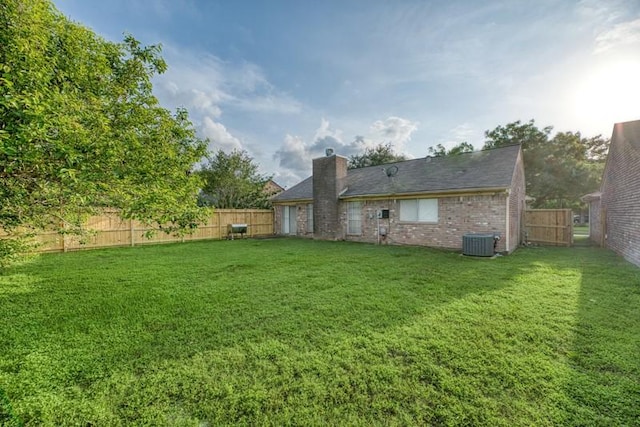 back of house featuring brick siding, a fenced backyard, a chimney, cooling unit, and a lawn