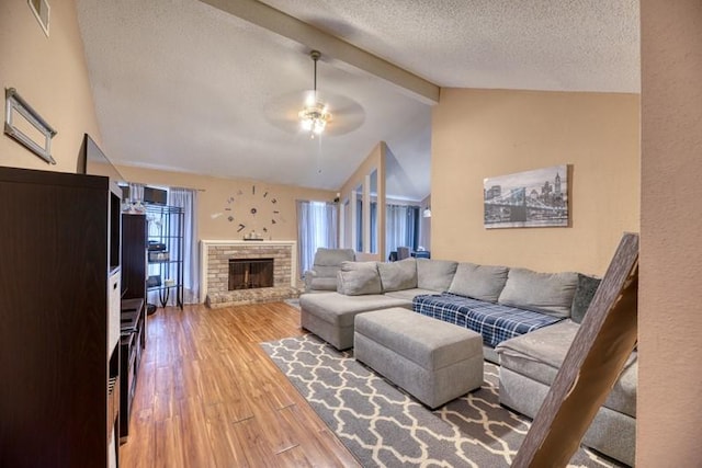 living area featuring visible vents, a brick fireplace, wood finished floors, ceiling fan, and lofted ceiling with beams