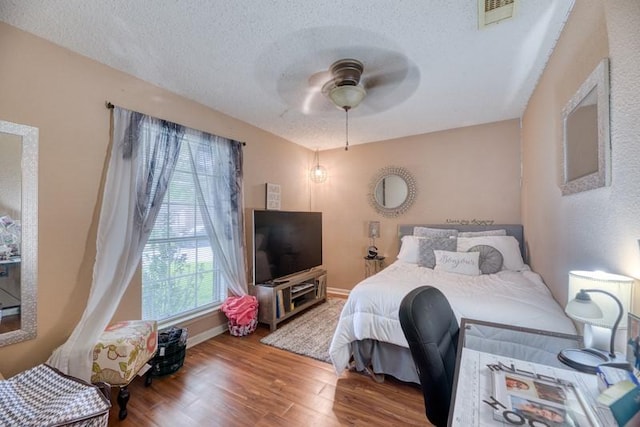 bedroom featuring visible vents, wood finished floors, baseboards, a textured ceiling, and a ceiling fan