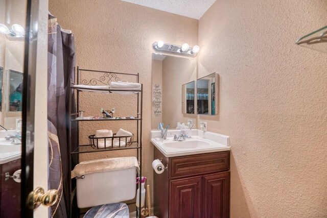 bathroom with toilet, a textured wall, and vanity