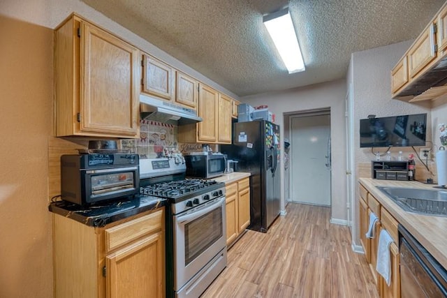 kitchen with light brown cabinets, light wood-style floors, a textured ceiling, under cabinet range hood, and stainless steel appliances