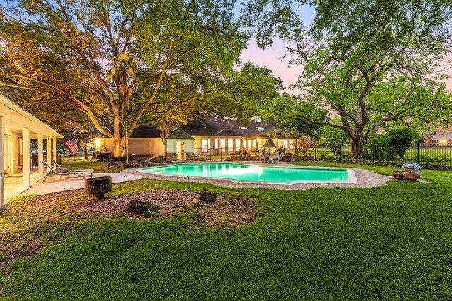 pool at dusk with a fenced in pool, fence, a yard, and a patio area