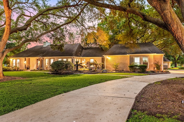 single story home with brick siding, curved driveway, a chimney, and a front lawn