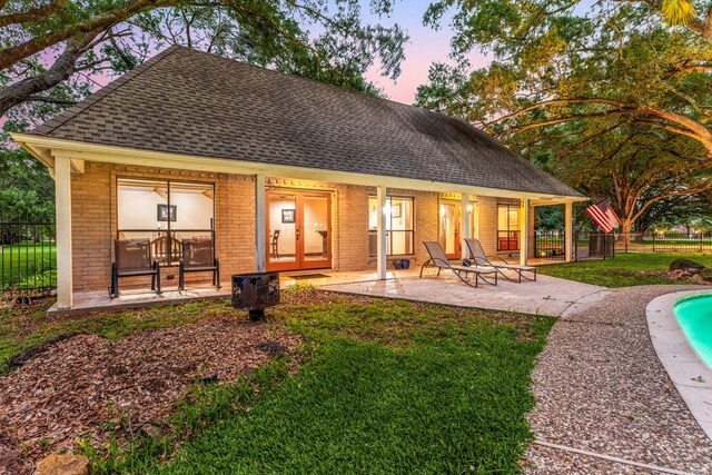 back of house at dusk featuring roof with shingles, fence, a fenced in pool, and brick siding