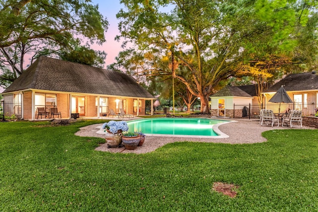 pool at dusk with a yard, a patio, and fence