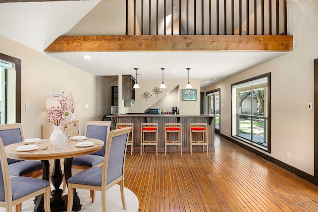 dining area featuring a towering ceiling, hardwood / wood-style flooring, baseboards, a bar, and recessed lighting