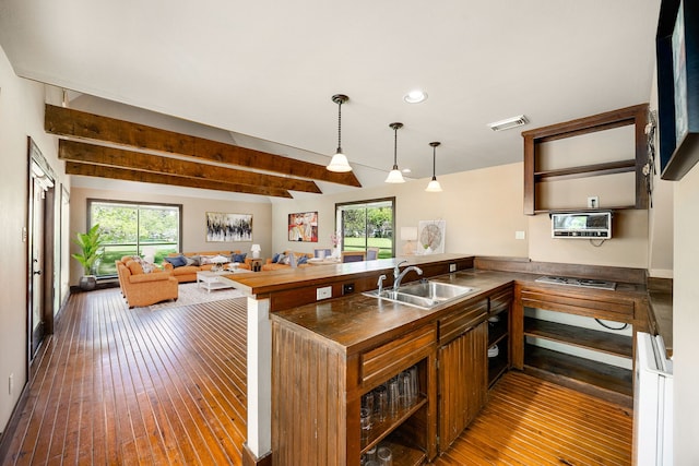 kitchen featuring visible vents, wood-type flooring, a peninsula, beamed ceiling, and a sink