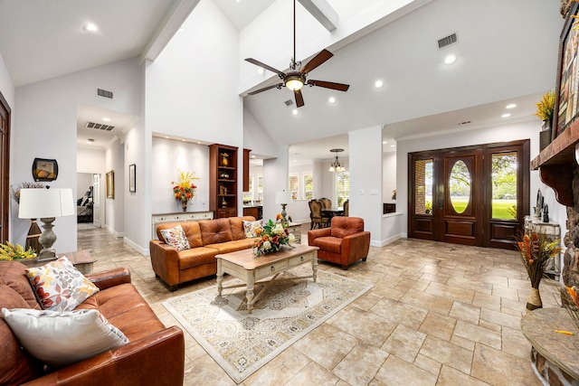 living area featuring visible vents, stone tile flooring, baseboards, high vaulted ceiling, and ceiling fan with notable chandelier