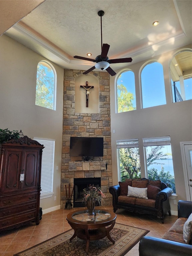 231 Key Largo Loop, Point Blank, TX 77364 - living room with light tile patterned flooring, a stone fireplace, ceiling fan, a high ceiling, and a raised ceiling