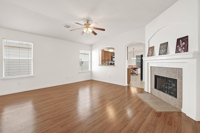 unfurnished living room with wood finished floors, ceiling fan, arched walkways, and baseboards