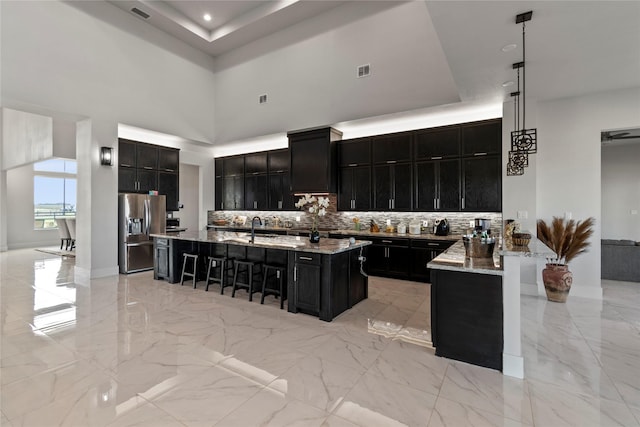 kitchen with dark cabinetry, stainless steel refrigerator with ice dispenser, a tray ceiling, and a breakfast bar
