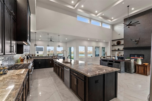 kitchen featuring light stone countertops, open floor plan, ceiling fan, a sink, and appliances with stainless steel finishes