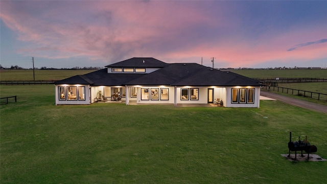 back of property at dusk with a lawn, a patio, a rural view, and fence