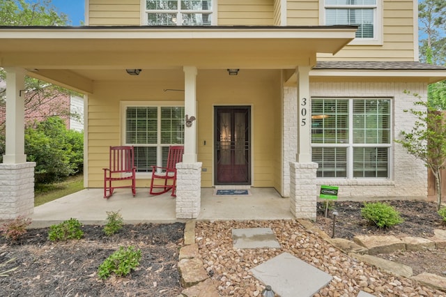 view of exterior entry featuring covered porch and brick siding