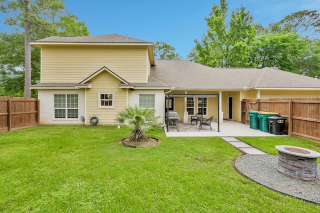 rear view of house featuring a fenced backyard, roof with shingles, a patio area, an outdoor fire pit, and a yard