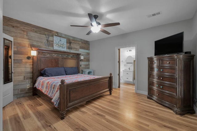 bedroom featuring ensuite bath, wood walls, a ceiling fan, light wood-type flooring, and visible vents