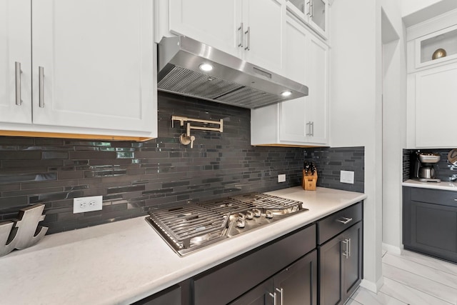 kitchen featuring under cabinet range hood, white cabinets, stainless steel gas stovetop, and light countertops