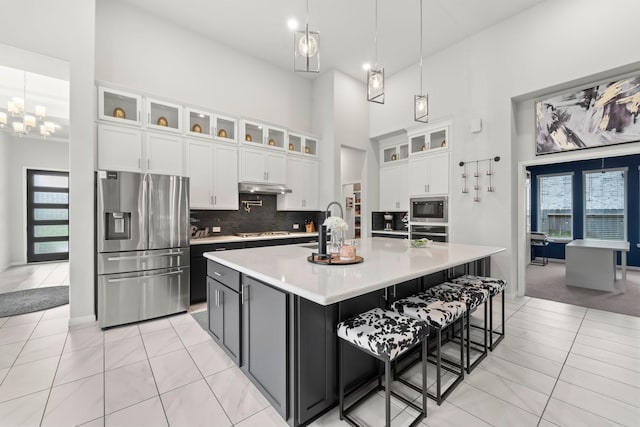 kitchen with a high ceiling, light countertops, under cabinet range hood, a sink, and stainless steel appliances