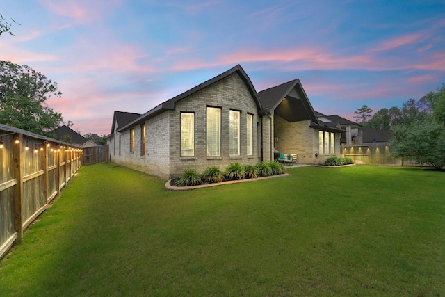 back of house at dusk with a fenced backyard, a yard, and brick siding