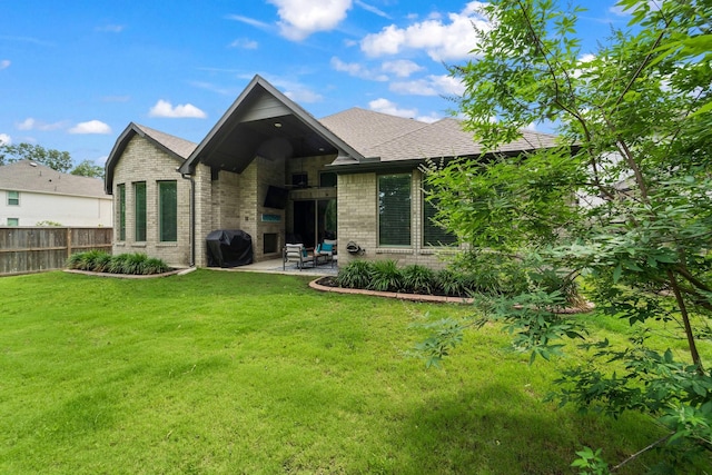 rear view of house featuring fence, roof with shingles, brick siding, a patio area, and a lawn