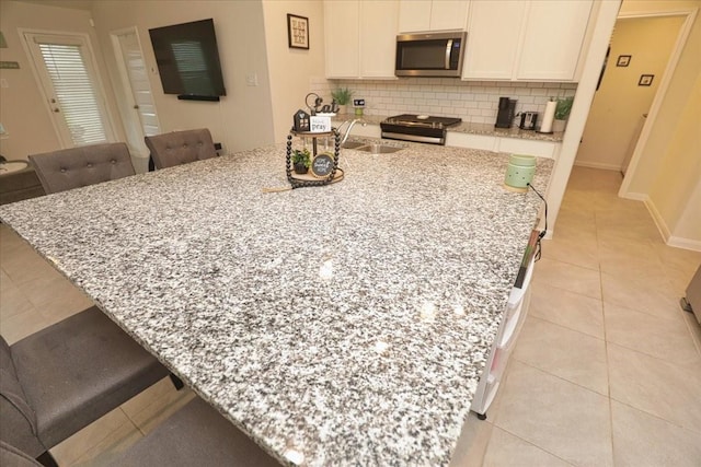 kitchen featuring appliances with stainless steel finishes, light stone counters, a breakfast bar area, light tile patterned floors, and backsplash