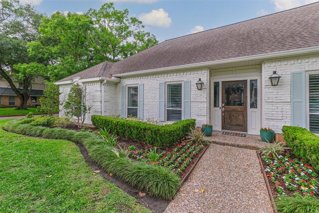 entrance to property with brick siding and a shingled roof