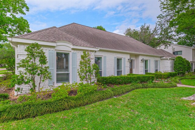 ranch-style home featuring a shingled roof, a front yard, and brick siding