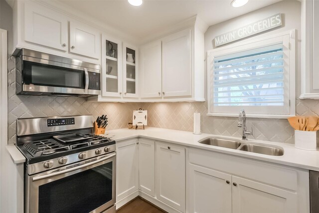 kitchen featuring white cabinets, appliances with stainless steel finishes, a sink, light countertops, and glass insert cabinets