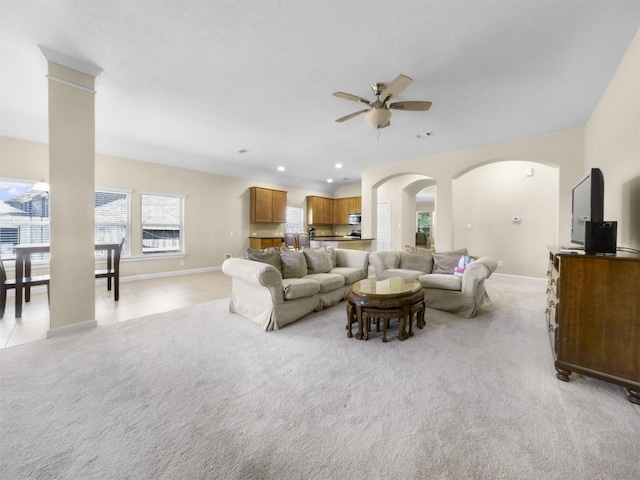 living room featuring light carpet, baseboards, a ceiling fan, and arched walkways