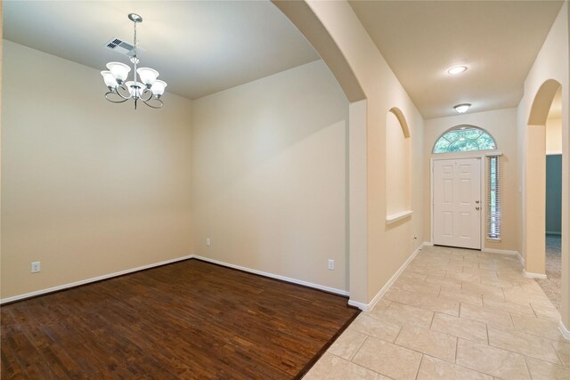 foyer with arched walkways, a chandelier, baseboards, wood finished floors, and visible vents
