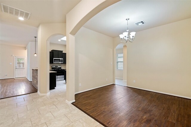 empty room with visible vents, arched walkways, baseboards, and light wood-type flooring