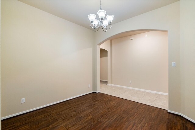 empty room featuring baseboards, arched walkways, wood finished floors, and a notable chandelier