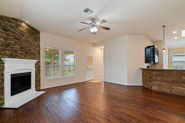 unfurnished living room with ceiling fan, a fireplace with raised hearth, baseboards, dark wood-type flooring, and visible vents