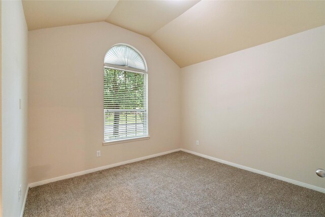 empty room with carpet flooring, baseboards, and vaulted ceiling