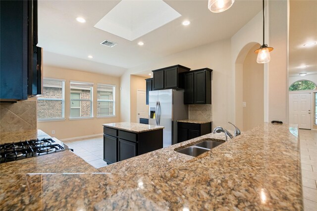 kitchen featuring a sink, arched walkways, decorative backsplash, light tile patterned floors, and stainless steel refrigerator with ice dispenser