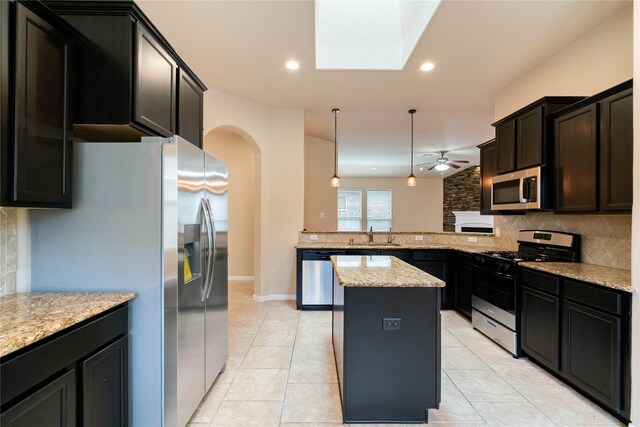 kitchen featuring appliances with stainless steel finishes, arched walkways, a center island, a peninsula, and backsplash