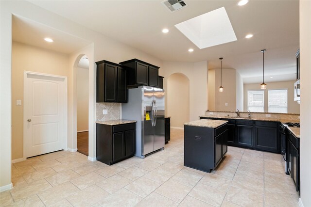 kitchen featuring visible vents, stainless steel refrigerator with ice dispenser, tasteful backsplash, arched walkways, and a skylight