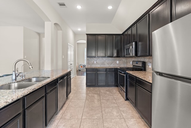 kitchen featuring visible vents, arched walkways, light stone counters, a sink, and stainless steel appliances