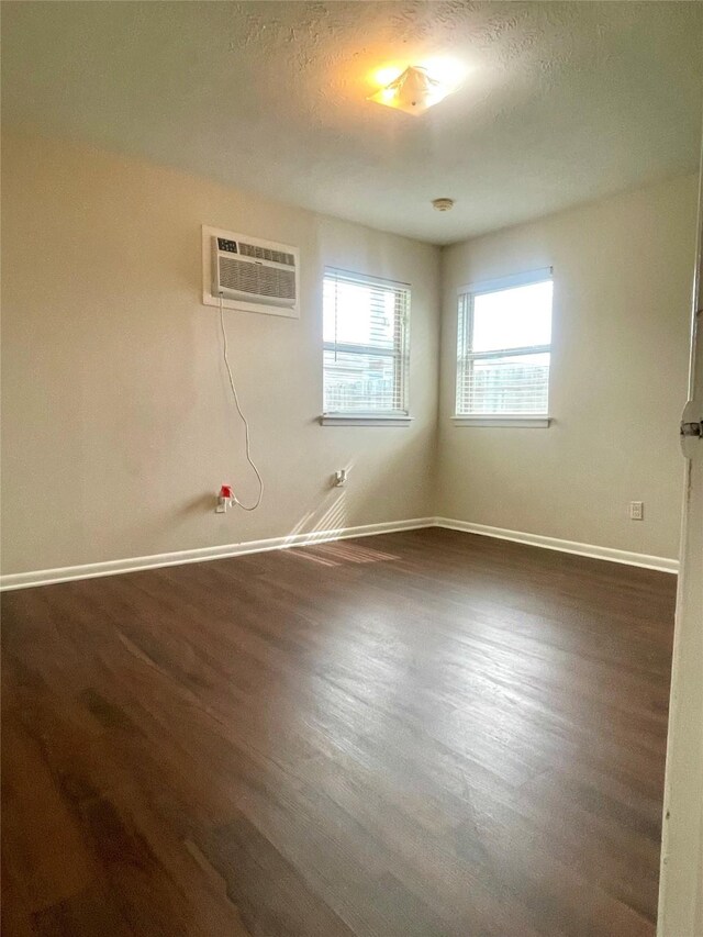 empty room with baseboards, a textured ceiling, a wall mounted AC, and dark wood-style floors