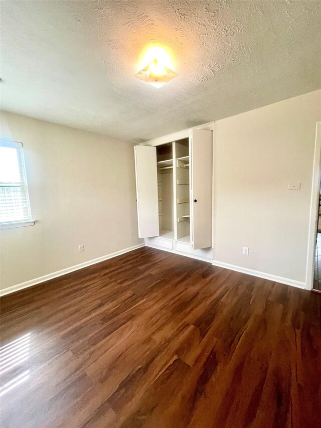 unfurnished bedroom with a closet, baseboards, a textured ceiling, and dark wood-type flooring