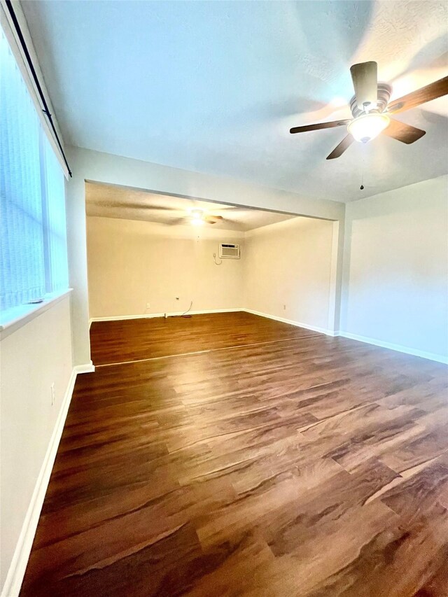 empty room featuring baseboards, a ceiling fan, a wall mounted AC, and wood finished floors
