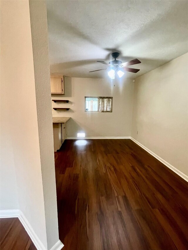 unfurnished living room featuring baseboards, ceiling fan, and dark wood-style floors