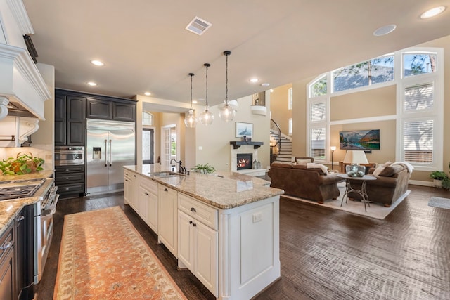 kitchen featuring light stone countertops, a sink, high end appliances, visible vents, and a center island with sink