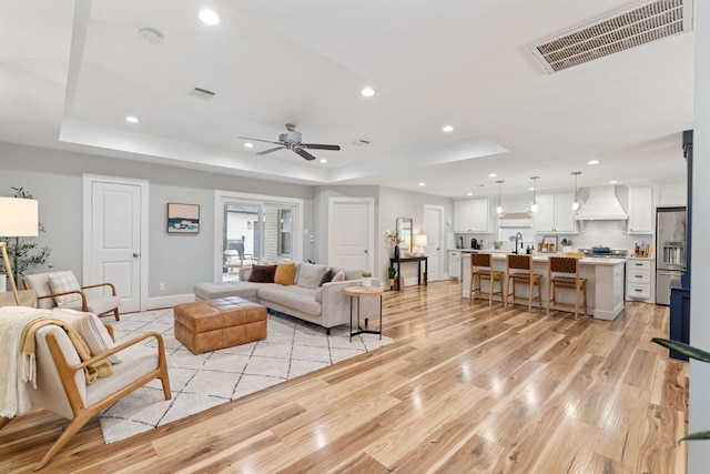 living room with a tray ceiling, recessed lighting, light wood-style flooring, and visible vents